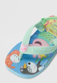 Flip-flop verde din cauciuc, cu o bază texturată albastră și personaje de desene animate colorate, inclusiv un purcel roz, și un accent decorativ roz.