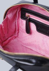 Interno della borsa nera con una fodera in tessuto rosa liscio, caratterizzato da un testo del logo del marchio ripetuto, una tasca con zip e dettagli della cerniera in tono oro.