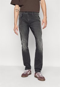 Fekete farmernadrág, slim fit szabásban, enyhe kopással, öt zsebes kialakítással és cipzáras záródással, bordó sportcipővel, fehér csíkokkal párosítva.
