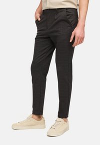 Mørke ternede bukser med skræddersyet pasform, lommer og en glat tekstur, kombineret med lyse beige sneakers.