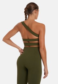 Olijfgroen geribbeld sporttop met een enkele schouderband en horizontale uitsparingen. Gecombineerd met hooggetailleerde geribbelde legging.
