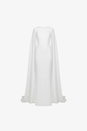 Fehér testhez simuló, földig érő ruha hosszú, áramló köpenyszerű ujjakkal és magas, kerek nyakkivágással, egyszerű háttéren bemutatva.