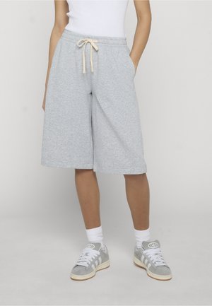 Osoba ubrana w jasnoszare sportowe spodenki do kolan z sznurkiem, białe skarpetki, szaro-białe sneakersy oraz biały top bez rękawów.