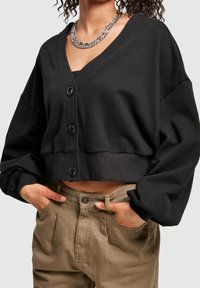 Black cropped cardigan with long, loose sleeves and a deep V-neck, featuring three large buttons at the front and a smooth texture.