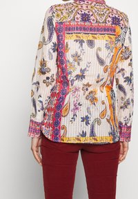 Blouse à motifs multicolores avec des designs floraux et cachemire, comprenant un col détaillé, des manches longues et des boutons en guise d'accent. Tissu texturé.