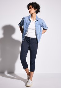 Dżinsowa kurtka i biała koszulka w zestawie z granatowymi, skróconymi spodniami. Sneakersy są białe z teksturowanym wykończeniem. Nowoczesny krój z luźnym fasonem.