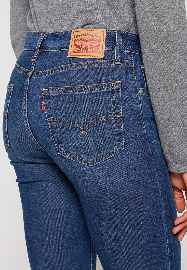 Dunkelblaue Jeans mit hoher Taille, ausgestattet mit einem Leder-Logo-Patch, zwei Gesäßtaschen und kontrastierenden Stickdetails.