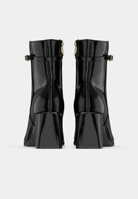 Mustad läikivad nahast pahkluusaapad, millel on plokkninad, sujuva tekstuuriga ja kullatoonilised pandlad pealispinnal, tagamaks kindla istuvuse.