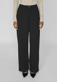 Pantalons larges noirs avec une texture lisse, dotés d'une fermeture à bouton à l'avant et sans motifs visibles. Associés à des chaussures noires à bout pointu.