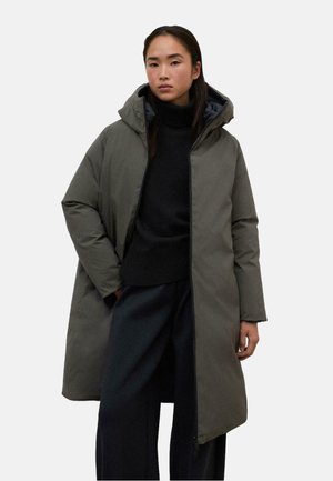 Abrigo acolchado de material gris oscuro, con capucha, cierre de cremallera y bolsillos laterales. Lleva puesto un cuello de tortuga negro y pantalones oscuros.