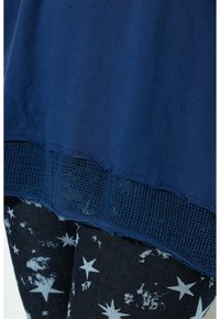 Top blu navy con orlo in rete testurizzato, indossato sopra un denim con un motivo a stelle in azzurro chiaro e una finitura ingrigita.
