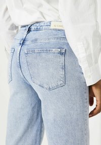Jeans de mezclilla azul claro con una textura ligeramente desgastada, con una cintura de tiro medio y bolsillos en la parte trasera. Etiqueta visible en la cinturilla.