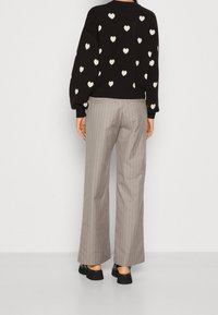 Schwarzer Pullover mit weißen Herzmustern, kombiniert mit grauen Streifen-Hosen mit weitem Bein und schwarzen Plateausandalen. Texturierte Stoffdetails sind sichtbar.