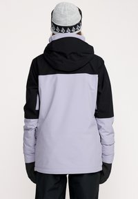 Tofarvet snejakke med en lavendel farvet krop, sorte detaljer og hætte. Stoffet ser glat ud med elastiske manchetter og sidelommer.