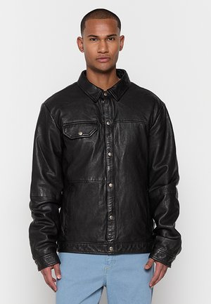 Chaqueta de cuero negro con cuello, cierre frontal a presión y bolsillo en el pecho. Presenta una textura suave y un ajuste relajado.