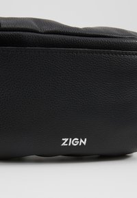 Pochette en cuir noir texturé avec le logo de la marque « ZIGN » imprimé en blanc au centre avant.