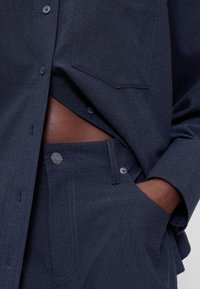 Marineblauw overhemd met knopen, gemaakt van gestructureerde stof, gecombineerd met bijpassende broek. Voorzien van een borstzak en zichtbare knoopdetails.