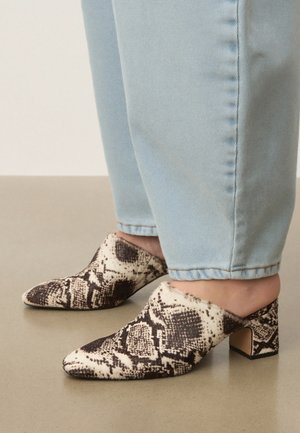 Noge v svetlo modrih kavbojkah in črno-belim škornjem z vzorcem kačje kože, z ostrim prstom in s srednje visokim podplatom.