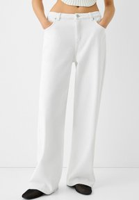 Vita högmidjade vida jeans med framfickor, knäppning och en ren design. Tyget verkar mjukt med minimal struktur.