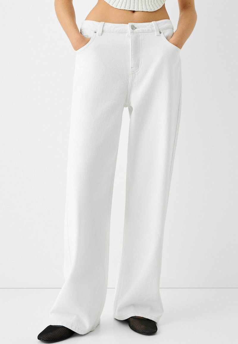 Vita högmidjade vida jeans med framfickor, knäppning och en ren design. Tyget verkar mjukt med minimal struktur.