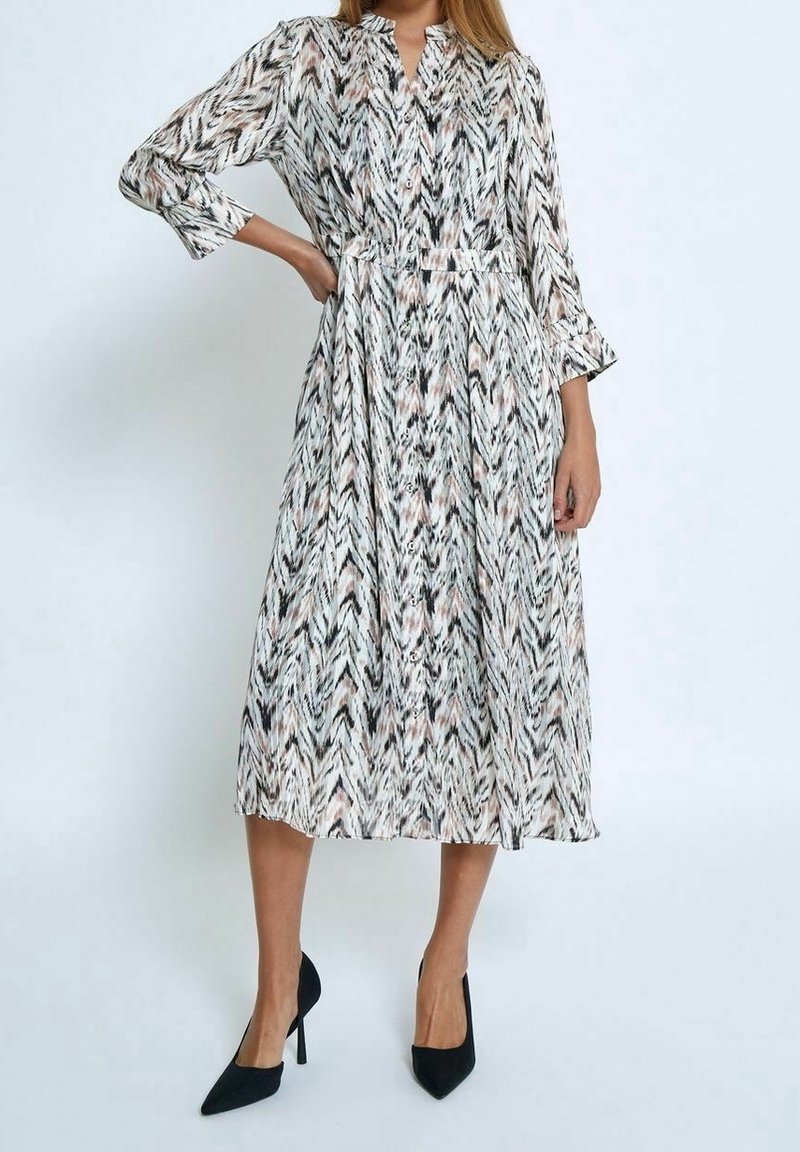 Robe midi à manches longues avec un motif chevron crème et noir, dotée de boutons, d'une ceinture à la taille et d'une jupe fluide.