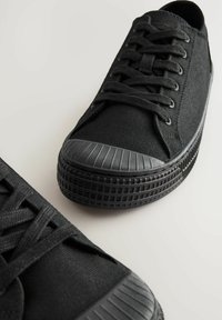 Sorte kanvas sneakers har en struktureret overflade, rund tå og en tyk gummisål med ribbede detaljer. Snørebånd løber gennem huller til lukning.