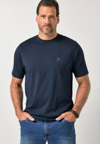 Marineblauw katoenen t-shirt met korte mouwen, ronde hals en een klein "JP" logo op de linkerborst. Gecombineerd met lichtblauwe spijkerbroek.