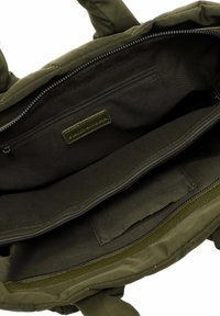 Green fabric bag interior showcasing a smooth texture with a zippered pocket, additional compartments, and a leather label.