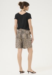 Zwarte t-shirt met korte mouwen en een V-vormige achterkant, gecombineerd met knie-lange shorts met luipaardprint, voorzien van zijzakken en een ontspannen pasvorm.