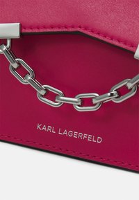 Różowa skórzana torebka z metalowym łańcuchem, z przeszytymi akcentami i brandingiem "KARL LAGERFELD" w metalicznym druku.
