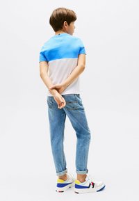 T-shirt a maniche corte con blocchi di colore blu e bianco, abbinato a jeans azzurri. L'outfit include sneaker bianche con accenti colorati.