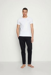 Λευκό κοντομάνικο μπλουζάκι και μαύρο στενό παντελόνι, κατασκευασμένα από μαλακό μείγμα βαμβακιού, με διακριτό λογότυπο στο στήθος.