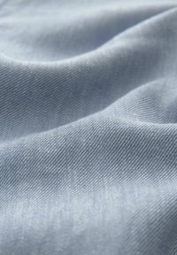 Light blue denim fabric with a soft texture, featuring a subtle twill weave and gentle ripples, creating an impression of movement.