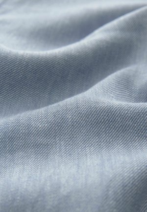Hellblaues Denim-Gewebe mit einer weichen Textur, das eine subtile Köperwebung und sanfte Wellen aufweist, die einen Eindruck von Bewegung erzeugen.