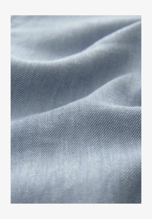 Hellblaues Denim-Gewebe mit einer weichen Textur, das eine subtile Köperwebung und sanfte Wellen aufweist, die einen Eindruck von Bewegung erzeugen.
