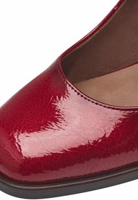 Chaussure plate en cuir rouge foncé brillant, avec un bout arrondi et des coutures apparentes le long du bord supérieur, et une semelle intérieure marron rembourrée.