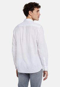 Chemise blanche à manches longues en tissu léger, dotée d'un col classique, de poignets à boutons et d'un pli dans le dos pour un confort de mouvement accru.