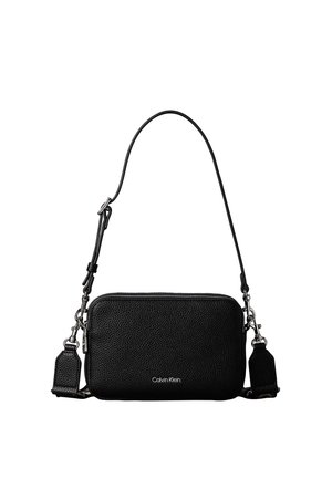 Sac bandoulière Calvin Klein en cuir noir texturé avec fermetures éclair argentées et bandoulière ajustable sur fond blanc.