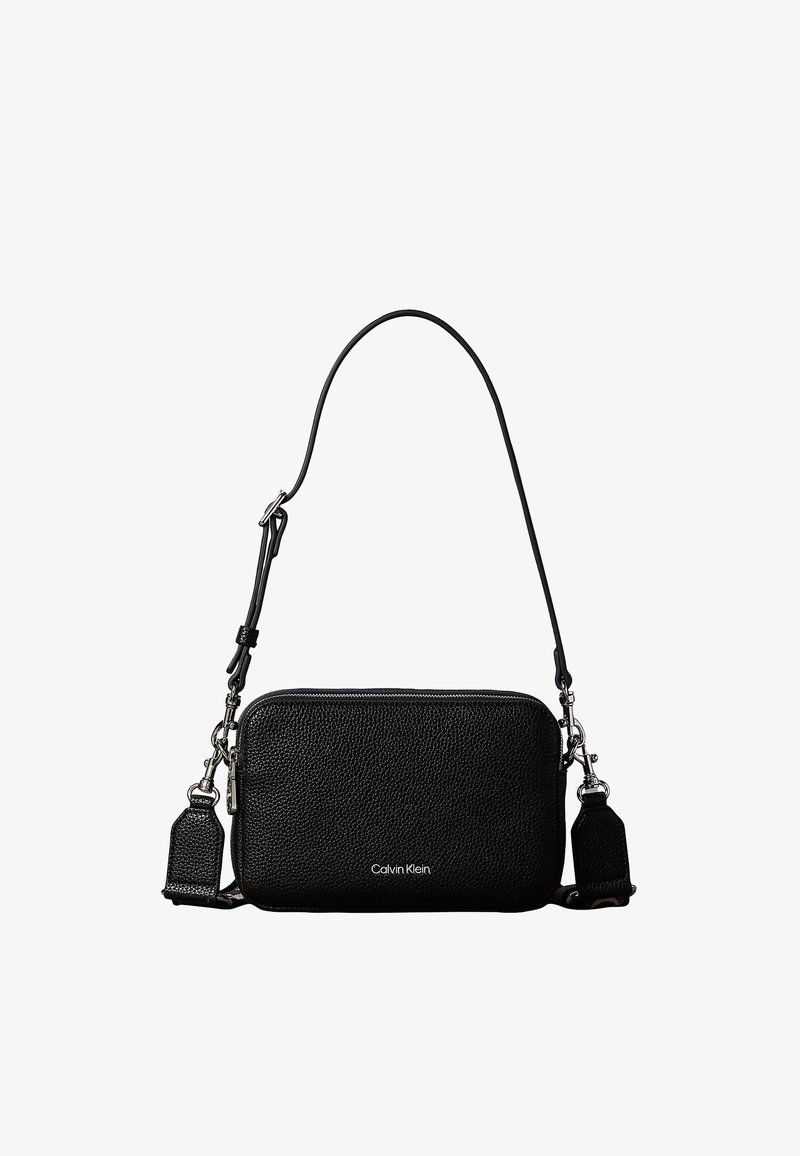 Μαύρη υφασμάτινη δερμάτινη τσάντα Calvin Klein α λα καρρέ με ασημένια φερμουάρ και ρυθμιζόμενο λουρί σε λευκό φόντο.