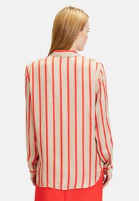 Beige blouse with vertical red stripes, long sleeves, and buttoned cuffs. Smooth texture, relaxed fit, and back collar detail visible.