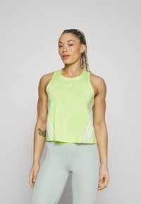 Neon groene sporttanktop met witte strepen, mouwloos ontwerp, ronde halslijn en zachte textuur, gecombineerd met lichtgroene leggings.