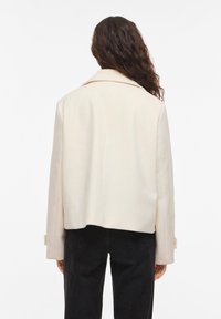 Κρεμ-χρωματιστό κοντό σακάκι με γιακά με εγκοπές και μακριά μανίκια. Με ομαλή υφή, μινιμαλιστικό σχέδιο, που δείχνει την πλάτη και τις λεπτομέρειες των μανικιών.