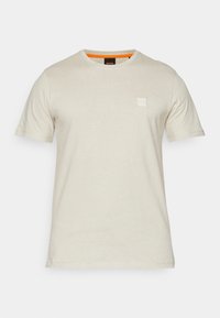 T-shirt beige à manches courtes avec col rond, petit logo carré sur la poitrine et bordure orange à l’intérieur du col.