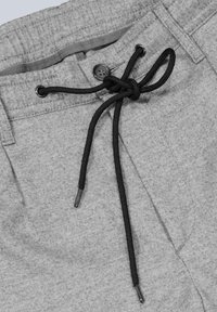 Graue Stoffhosen mit einem schwarzen Kordelzug, der in einer Schleife nahe einem Knopf und den Gürtelschlaufen am Bund gebunden ist.