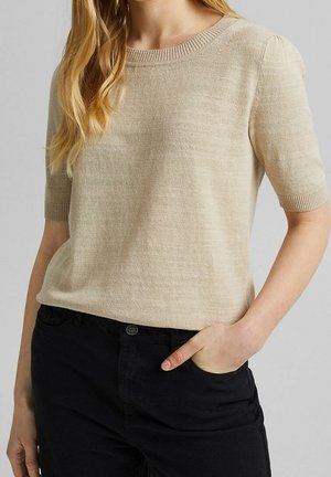 Beige kortærmet sweater med rund halsudskæring, ribbede manchetter og glat tekstur, kombineret med sorte bukser.