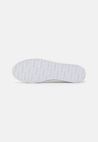 Semelle de chaussure blanche avec texte répété "TOMMY" et motifs de cœur embossés sur la surface inférieure.