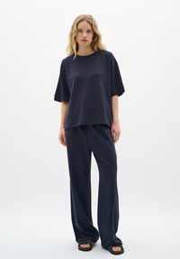 Navy színű, rövid ujjú, laza fazonú felső, széles lábú navy nadrággal párosítva. Mindkét ruhadarab sima textúrával és laza stílussal rendelkezik.