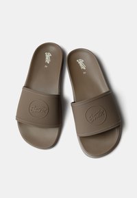 Sandales en caoutchouc marron avec une bride texturée arborant un logo circulaire, semelle plate et design minimaliste. Taille indiquée comme 42.