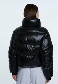 Giacca a vento nera con colletto alto, design trapuntato e finitura lucida. Presenta polsini elasticizzati e una silhouette cropped.