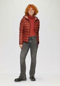 Czerwona kurtka puchowa z kapturem, pikowana konstrukcja. Noszona na rdzawym golfie, w zestawieniu z szarymi dżinsami i czarnymi masywnymi butami.